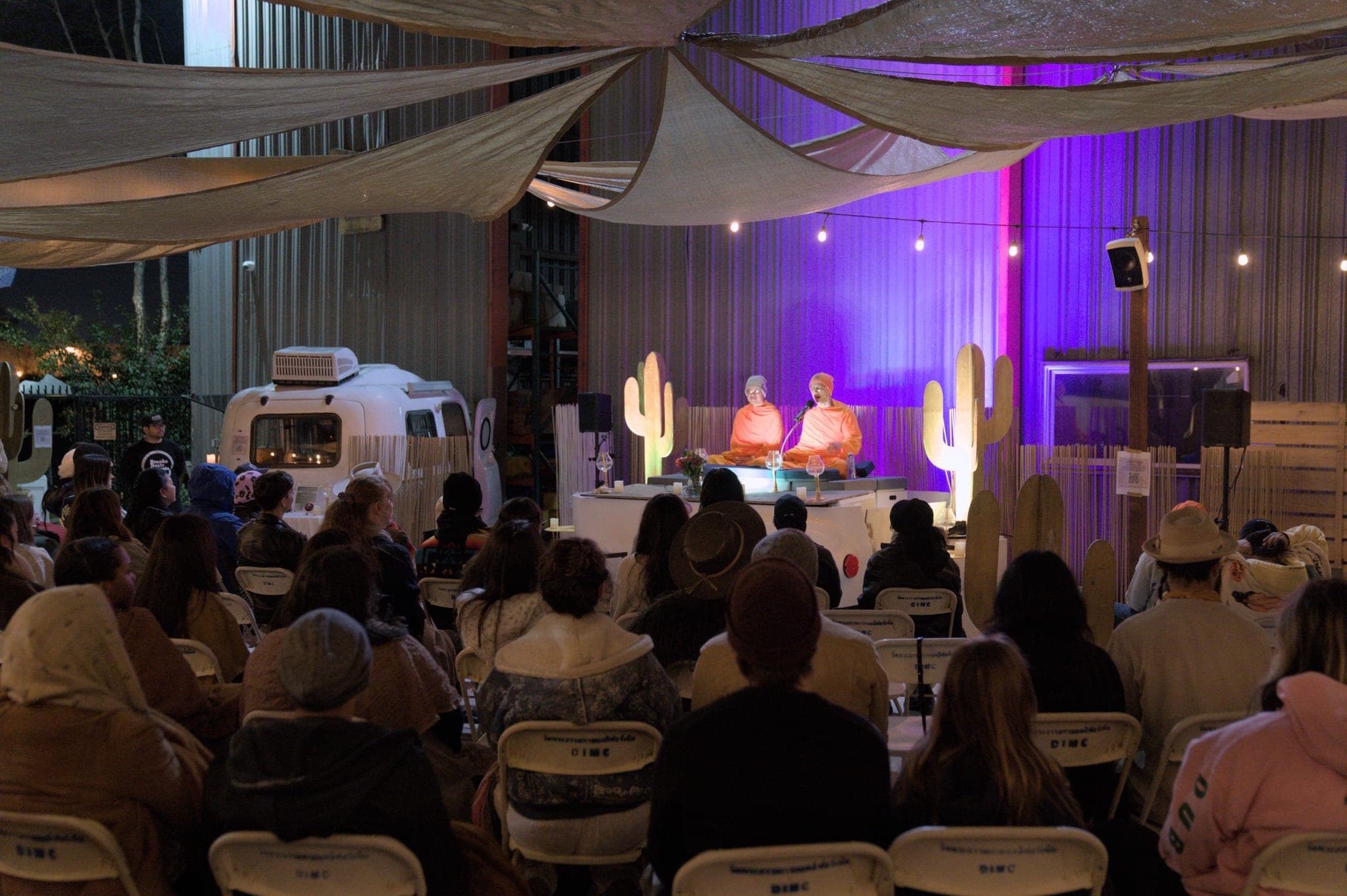 An indoor hall under draped fabric, guests seated facing two monks at the front.