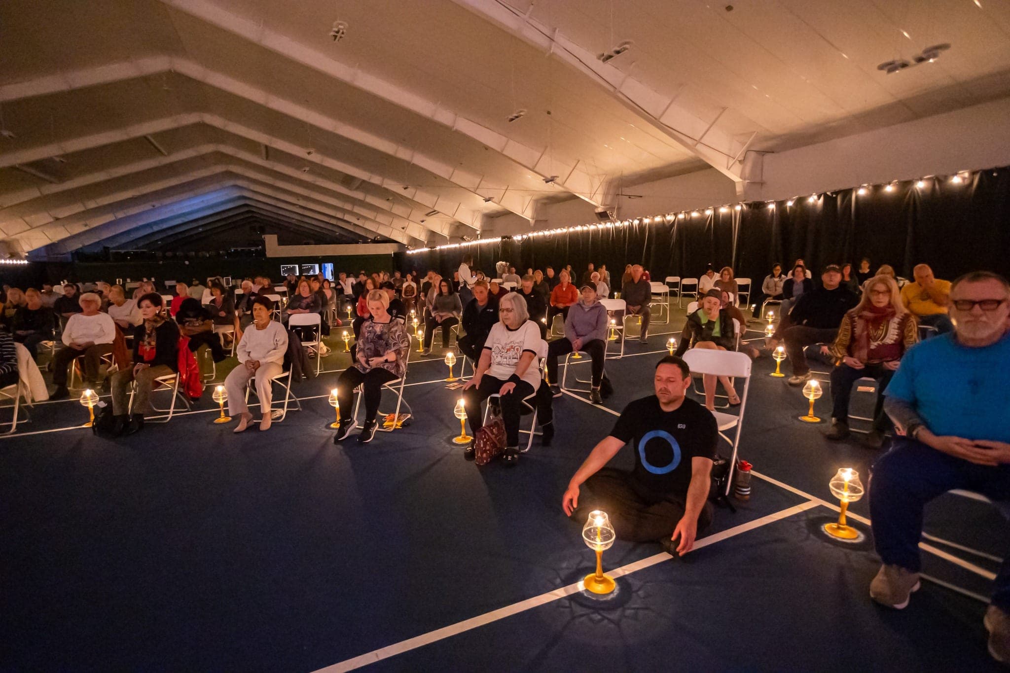 A large indoor space with guests seated in rows, a candle lamp set on the floor at each chair.