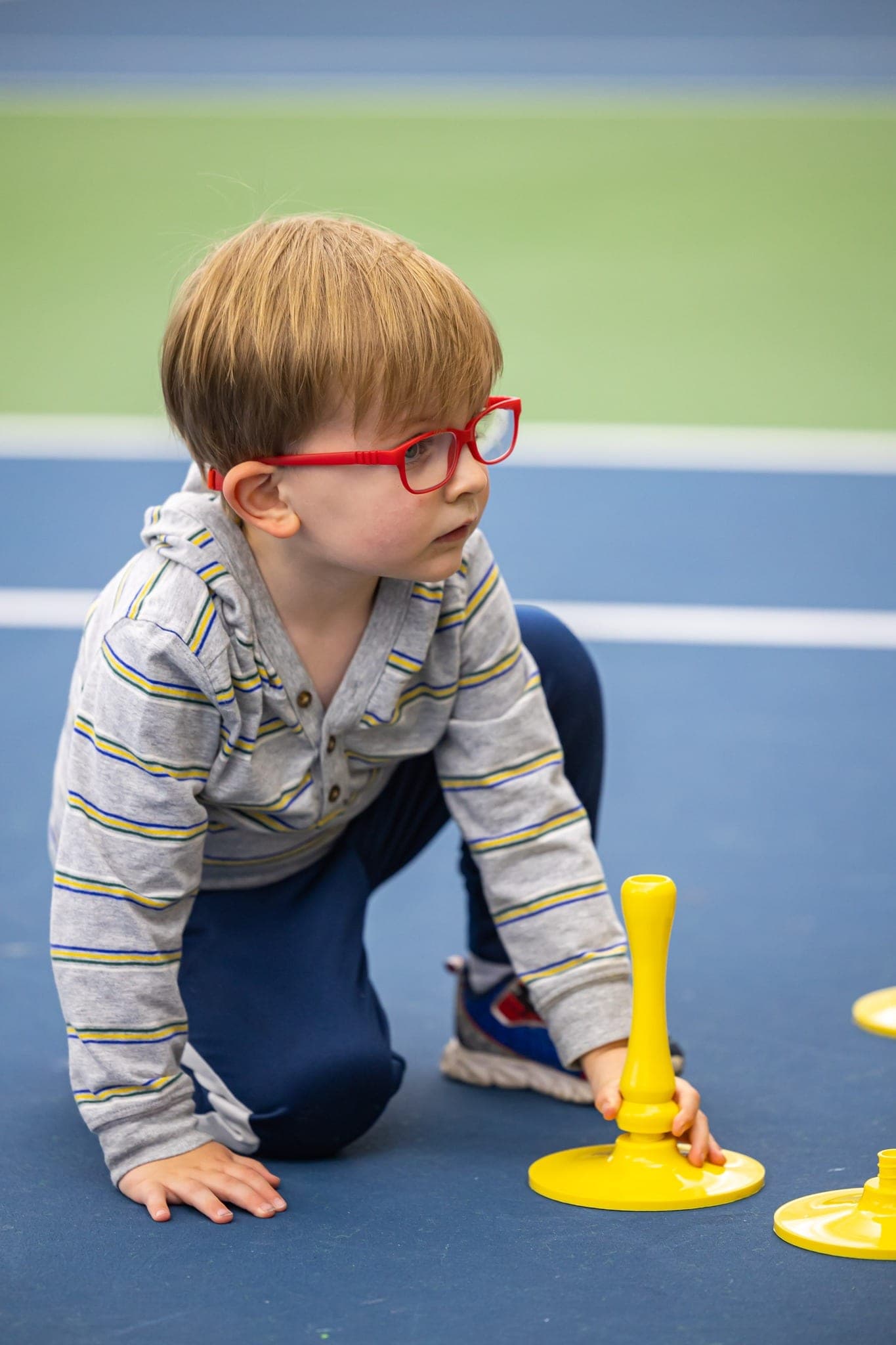 A small child in red glasses kneeling on a blue court beside a candle holder.