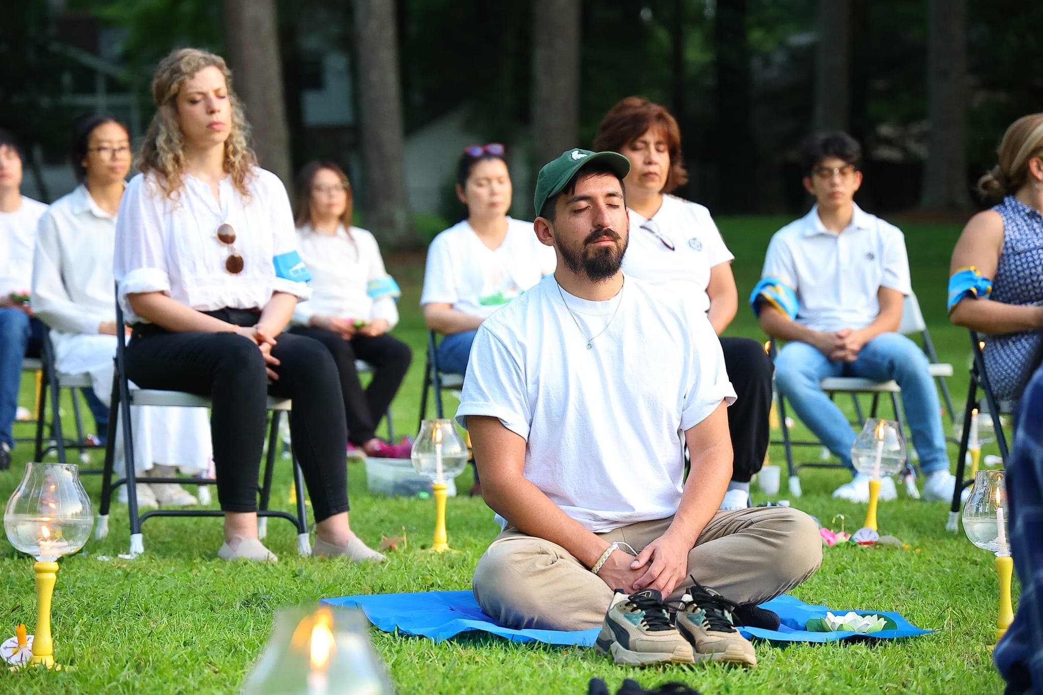 Guests meditating on mats and chairs on a lawn, candle lamps set beside them.