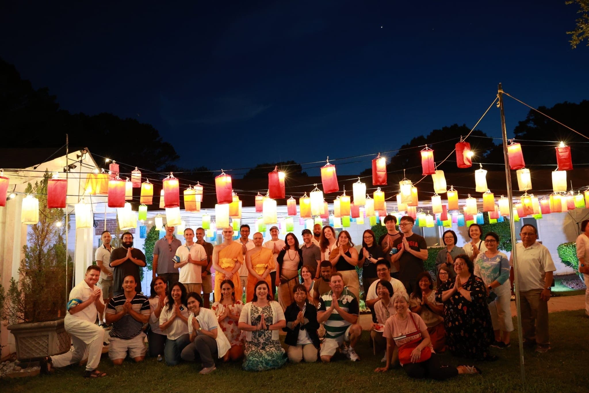 A group photograph at dusk in front of a wall of hanging lanterns.