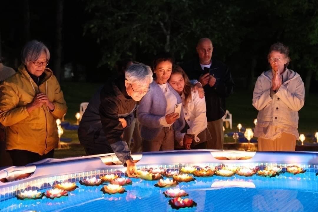 Guests standing in prayer at the edge of a pool of floating lotus candles.