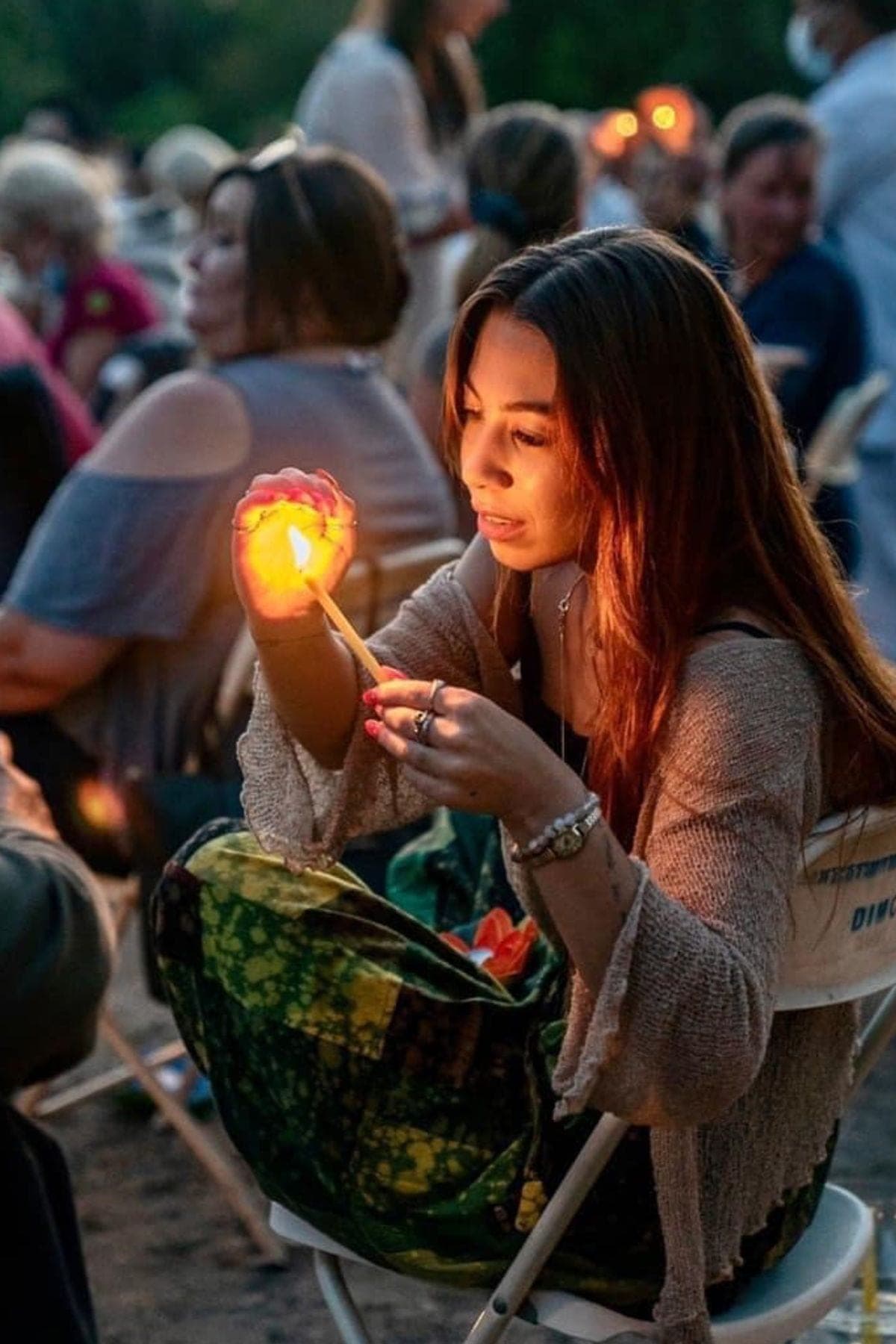A young woman crouching by the water, holding a lotus candle in both hands.