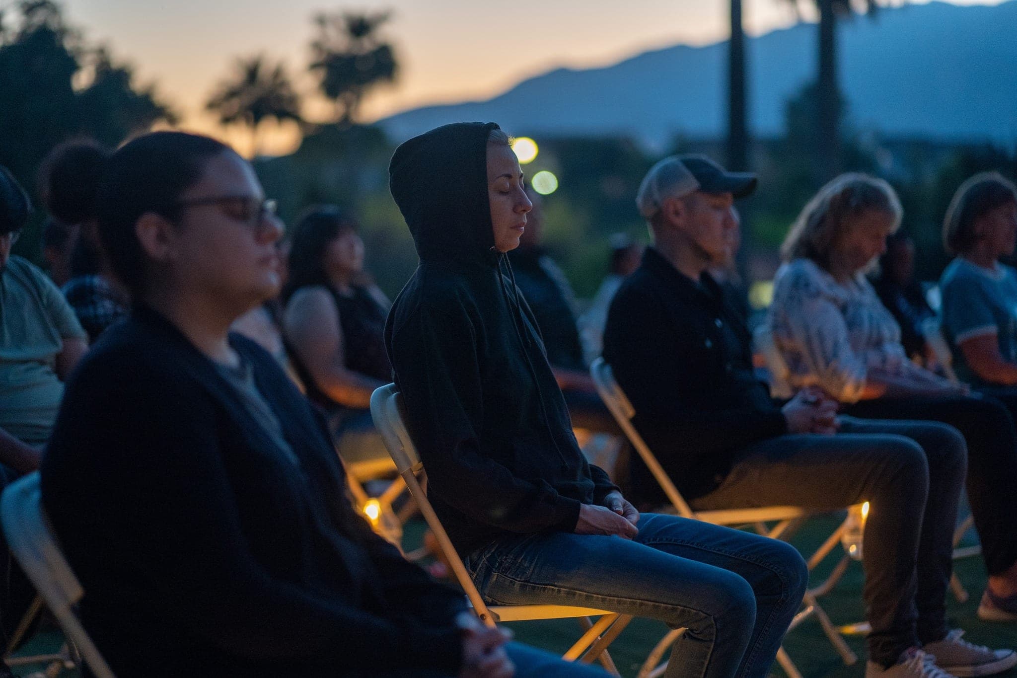 Guests seated in a row at dusk, a candle burning at each chair.