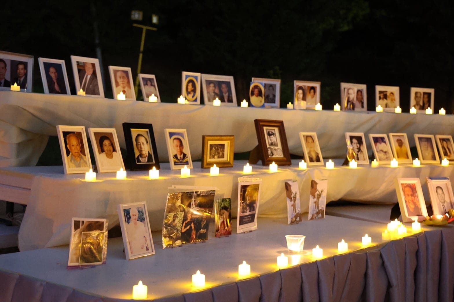 A long white table lined with framed photographs of departed loved ones, a candle burning beside each row.