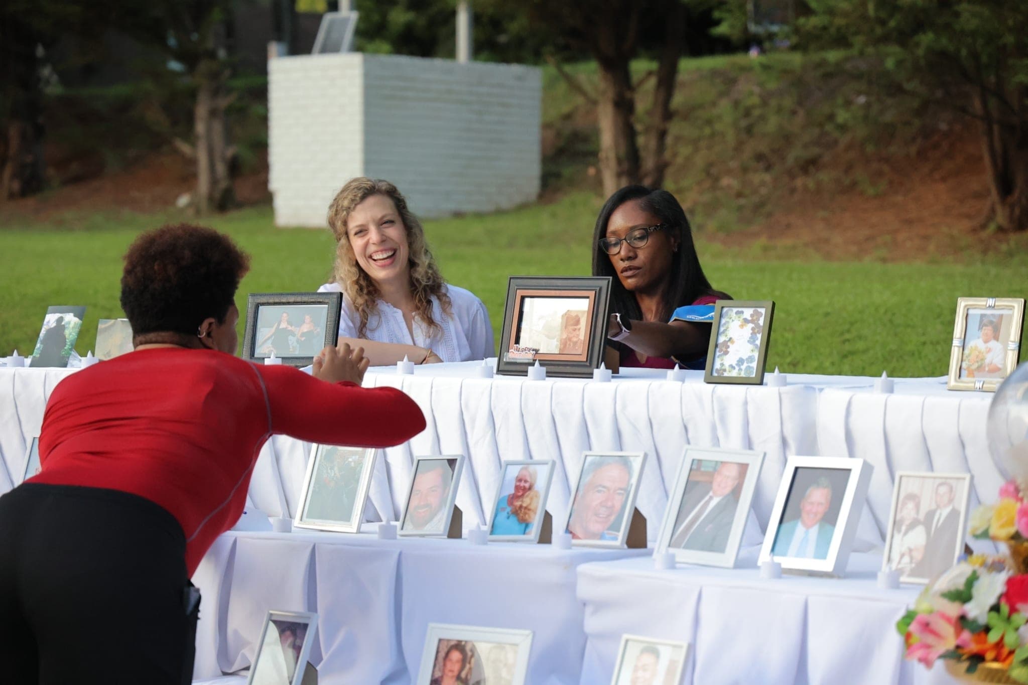 Volunteers setting framed photographs out along the memorial table on a lawn.