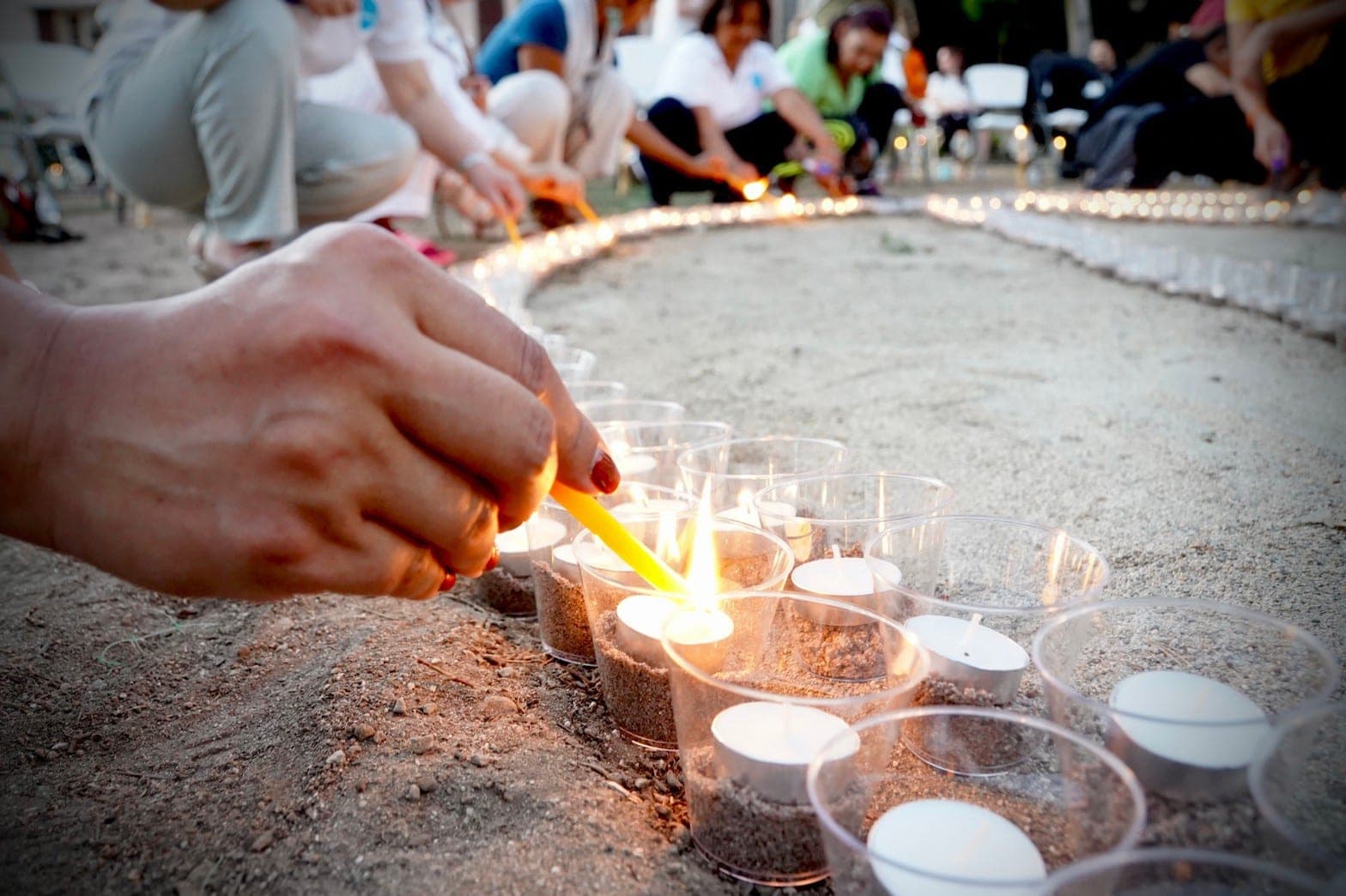 A hand lighting a candle in a long curving line of tea lights.