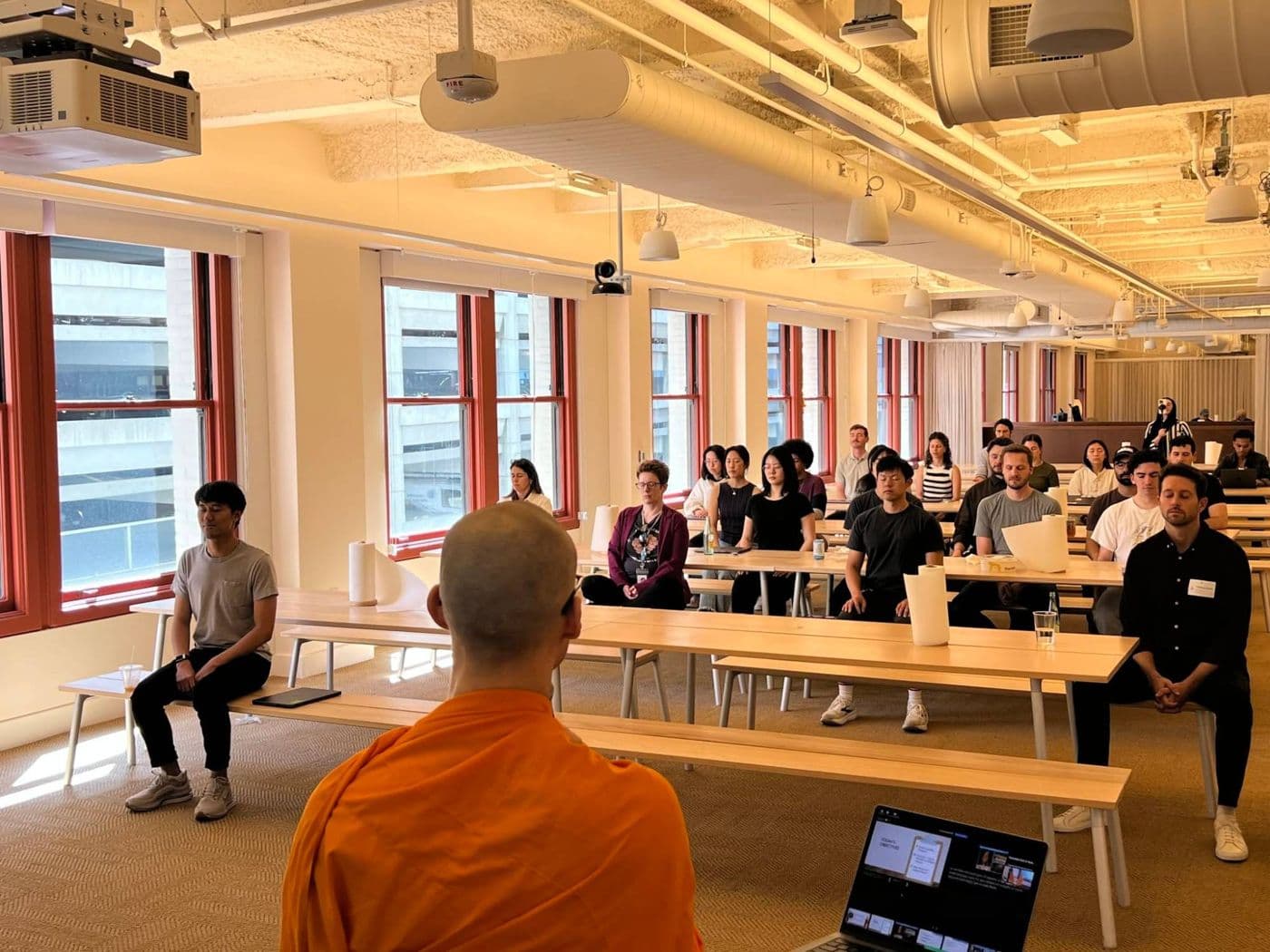 Notion employees meditating at long tables while a monk guides them from the front