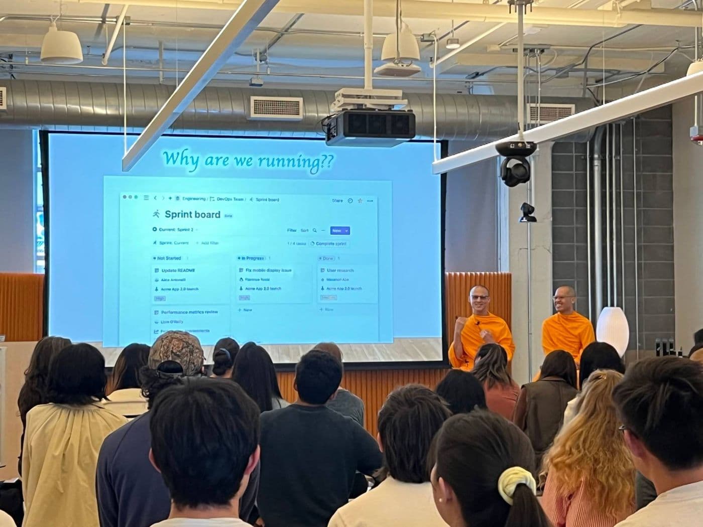 The monks presenting to a full room under a slide reading Why are we running?
