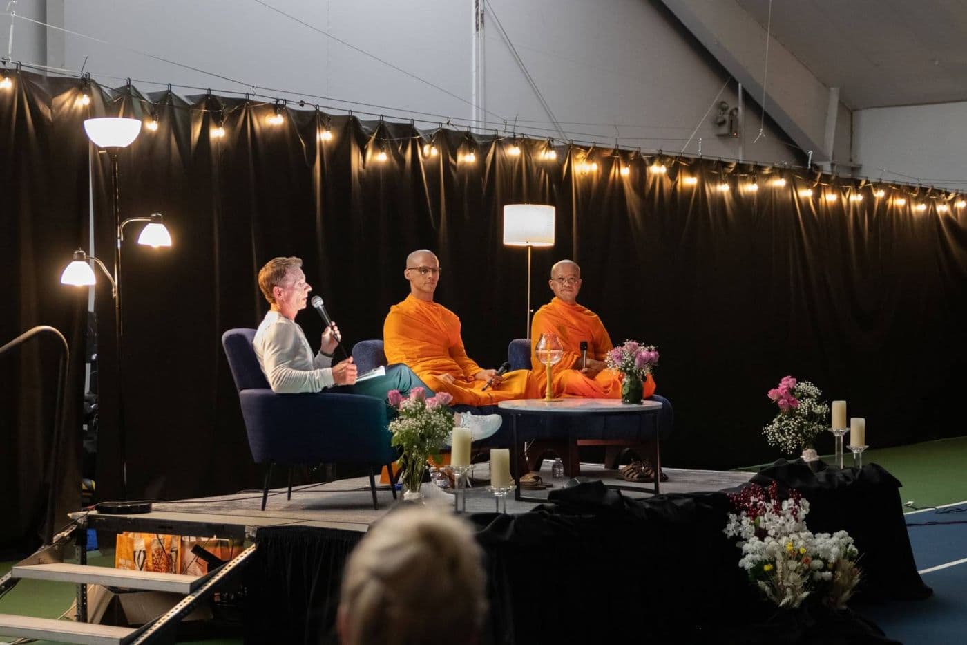 George Zink with a microphone beside the two monks on a candlelit stage