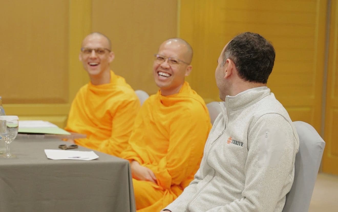 The monks laughing at a table with a member of the Thrive team