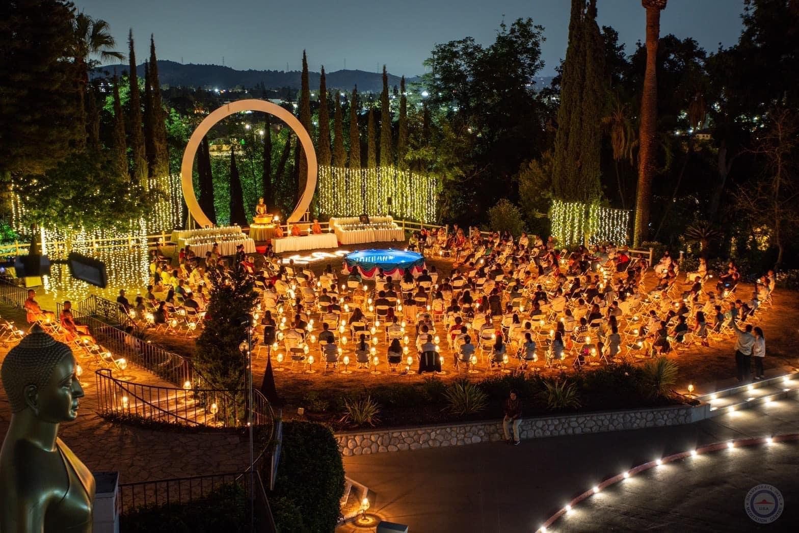 A candlelight meditation event at dusk: rings of candles and seated guests across a terraced garden lawn, with a lit archway at one end.