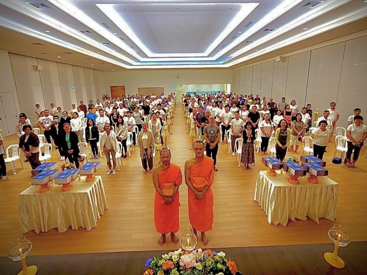 A large hall of event participants, with tables of books set out in front of the monks.