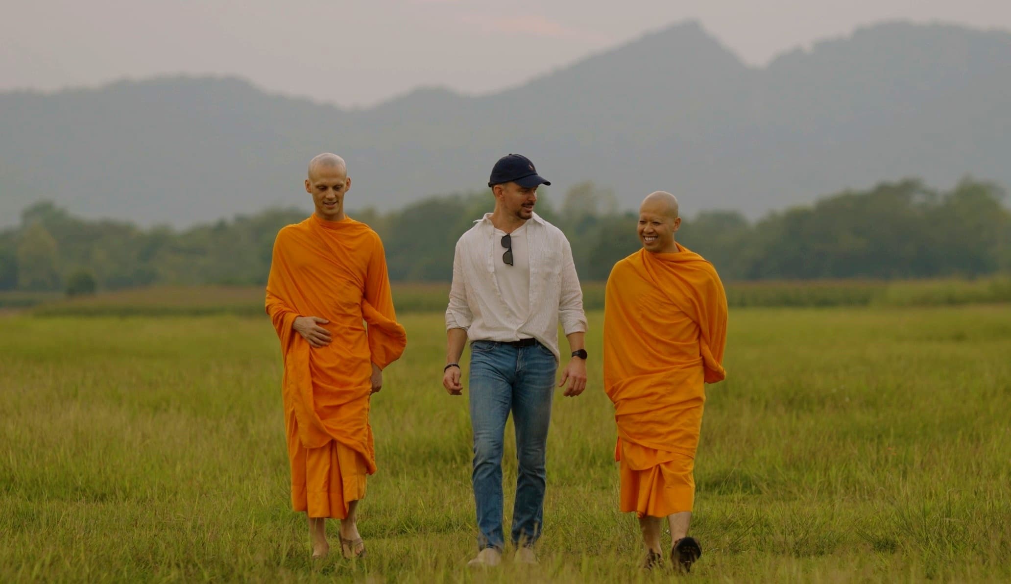 Two monks walking through a misty field alongside a layperson.